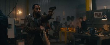 Movie still from “Nobody” (2021), directed by Ilya Naishuller – A man holding a gun in a room with other people; Medium shot, Over the shoulder angle