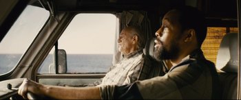 Movie still from “Nobody” (2021), directed by Ilya Naishuller – Two men sitting in a vehicle looking out the window; Medium shot, Over the shoulder angle