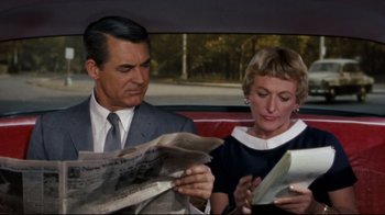 Movie still from “North by Northwest” (1959), directed by Alfred Hitchcock – A man and a woman sitting in the back seat of a car reading newspapers; Medium shot, Over the shoulder angle