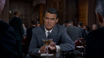 Movie still from “North by Northwest” (1959), directed by Alfred Hitchcock – A man sitting at a table with a glass of wine; Medium shot, Over the shoulder angle