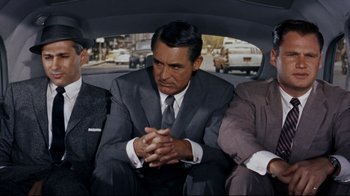 Movie still from “North by Northwest” (1959), directed by Alfred Hitchcock – A man in a suit sitting in the back of a car; Medium shot, High angle
