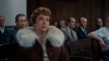 Movie still from “North by Northwest” (1959), directed by Alfred Hitchcock – An older woman wearing a fur coat in front of a group of people; Medium shot, Over the shoulder angle
