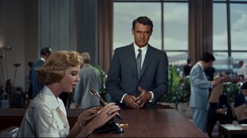 Movie still from “North by Northwest” (1959), directed by Alfred Hitchcock – A man in a suit and tie standing next to a woman in a white dress; Medium shot, Over the shoulder angle