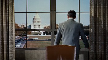 Movie still from “North by Northwest” (1959), directed by Alfred Hitchcock – A man in a suit looking out a window at the capitol building; Wide shot, Low angle