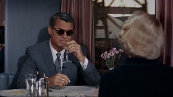 Movie still from “North by Northwest” (1959), directed by Alfred Hitchcock – An older man sitting at a table with a glass of wine in front of him; Medium shot, Over the shoulder angle