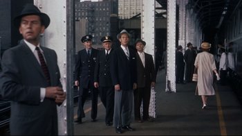Movie still from “North by Northwest” (1959), directed by Alfred Hitchcock – A group of men in suits and hats walking on a sidewalk; Wide shot, Low angle