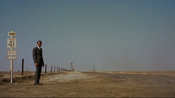 Movie still from “North by Northwest” (1959), directed by Alfred Hitchcock – A man standing on a dirt road near a fence; Wide shot, Low angle