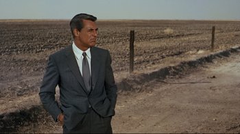 Movie still from “North by Northwest” (1959), directed by Alfred Hitchcock – A man in a suit and tie standing in the middle of an empty field; Medium shot, Over the shoulder angle