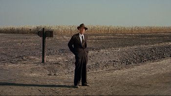 Movie still from “North by Northwest” (1959), directed by Alfred Hitchcock – A man in a suit and hat standing next to a wooden sign; Wide shot, High angle