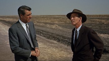 Movie still from “North by Northwest” (1959), directed by Alfred Hitchcock – A man in a suit and a man in a hat talking to each other in an open field; Medium shot, Over the shoulder angle