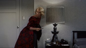 Movie still from “North by Northwest” (1959), directed by Alfred Hitchcock – A woman in a red and black dress looking at a remote control; Medium shot, High angle