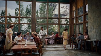 Movie still from “North by Northwest” (1959), directed by Alfred Hitchcock – People are sitting and standing at tables in a restaurant; Wide shot, Over the shoulder angle