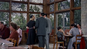 Movie still from “North by Northwest” (1959), directed by Alfred Hitchcock – A group of people standing in a room with windows; Wide shot, Over the shoulder angle