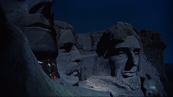 Movie still from “North by Northwest” (1959), directed by Alfred Hitchcock – A man standing on top of a mountain next to a statue; Extreme Wide shot, Low angle