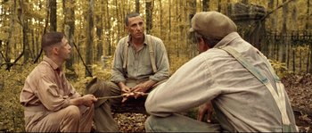 Movie still from “O Brother, Where Art Thou?” (2000), directed by Joel Coen – A man sitting on the ground in the woods; Medium shot, Over the shoulder angle