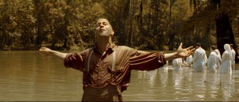 Movie still from “O Brother, Where Art Thou?” (2000), directed by Joel Coen – A man standing in the middle of a body of water with his arms outstretched; Medium shot, Low angle