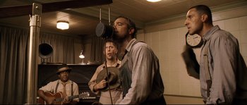 Movie still from “O Brother, Where Art Thou?” (2000), directed by Joel Coen – Two men are standing in a room and one of them is singing; Medium shot, Low angle
