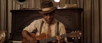Movie still from “O Brother, Where Art Thou?” (2000), directed by Joel Coen – A man in a hat playing a guitar; Medium shot, High angle