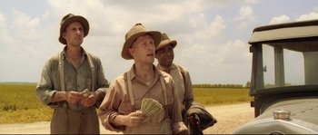 Movie still from “O Brother, Where Art Thou?” (2000), directed by Joel Coen – A man holding a bunch of money while standing next to another man; Medium shot, Low angle