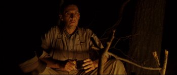 Movie still from “O Brother, Where Art Thou?” (2000), directed by Joel Coen – A man sitting in a dark room holding a cell phone; Medium shot, Low angle