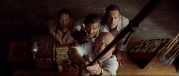 Movie still from “O Brother, Where Art Thou?” (2000), directed by Joel Coen – A group of men holding a baseball bat in a room; Medium shot, Overhead angle
