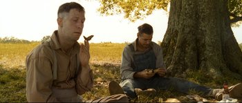 Movie still from “O Brother, Where Art Thou?” (2000), directed by Joel Coen – Two men sitting under a tree eating food; Medium shot, Low angle