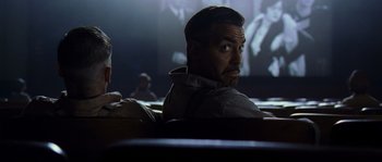 Movie still from “O Brother, Where Art Thou?” (2000), directed by Joel Coen – A man sitting in front of a projector screen in a theater; Medium shot, Low angle