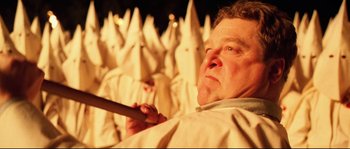 Movie still from “O Brother, Where Art Thou?” (2000), directed by Joel Coen – A man holding a wooden stick in front of a group of people in white robes; Close Up shot, High angle