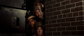 Movie still from “O Brother, Where Art Thou?” (2000), directed by Joel Coen – A group of men standing next to a brick wall; Medium shot, Low angle