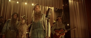 Movie still from “O Brother, Where Art Thou?” (2000), directed by Joel Coen – A man with a long beard singing into a microphone while another man plays a guitar; Medium shot, Low angle