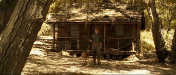 Movie still from “O Brother, Where Art Thou?” (2000), directed by Joel Coen – A man and a dog standing in front of a log cabin; Wide shot, Low angle