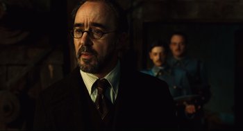 Movie still from “Pan's Labyrinth” (2006), directed by Guillermo del Toro – A man in a suit and tie standing in front of two other men; Close Up shot, Over the shoulder angle