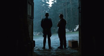 Movie still from “Pan's Labyrinth” (2006), directed by Guillermo del Toro – Two men are standing in the rain looking out a window; Wide shot, Over the shoulder angle