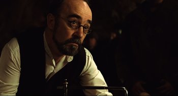 Movie still from “Pan's Labyrinth” (2006), directed by Guillermo del Toro – A man with a goatee and glasses is sitting at a table; Close Up shot, Over the shoulder angle