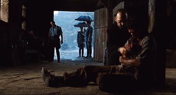 Movie still from “Pan's Labyrinth” (2006), directed by Guillermo del Toro – A group of people standing around a building with an umbrella; Wide shot, Over the shoulder angle