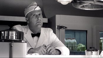 Movie still from “Pleasantville” (1998), directed by Gary Ross – A man wearing a white suit and a white hat sitting at a table; Medium shot, Low angle