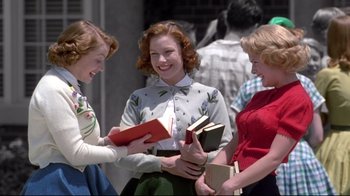 Movie still from “Pleasantville” (1998), directed by Gary Ross – A group of young women standing next to each other holding books; Medium shot, Low angle