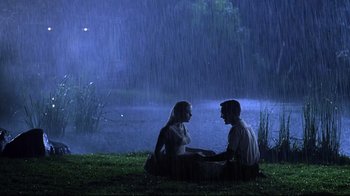 Movie still from “Pleasantville” (1998), directed by Gary Ross – A man and a woman sitting on the grass in the rain; Wide shot, High angle