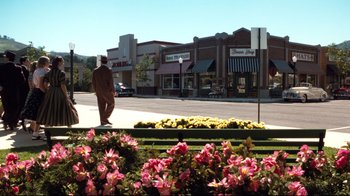 Movie still from “Pleasantville” (1998), directed by Gary Ross – A man walking down the sidewalk in front of stores; Extreme Wide shot, High angle