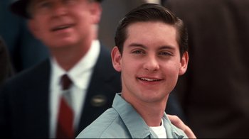 Movie still from “Pleasantville” (1998), directed by Gary Ross – A young man smiling for the camera while a man in a suit stands next to him; Close Up shot, Over the shoulder angle