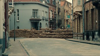 Movie still from “Dunkirk” (2017), directed by Christopher Nolan – An empty street in a european city with sandbags on the ground; Extreme Wide shot, High angle