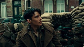Movie still from “Dunkirk” (2017), directed by Christopher Nolan – A young man in a trench coat is looking off into the distance; Close Up shot, Over the shoulder angle