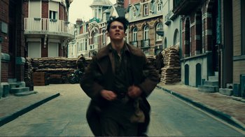 Movie still from “Dunkirk” (2017), directed by Christopher Nolan – A man in a trench coat walking down a street; Medium shot, Low angle