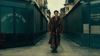 Movie still from “Dunkirk” (2017), directed by Christopher Nolan – A man in a long coat walking down a street; Wide shot, Low angle