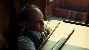 Movie still from “Dunkirk” (2017), directed by Christopher Nolan – A man sitting in front of a wooden table; Medium shot, High angle