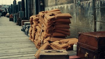 Movie still from “Dunkirk” (2017), directed by Christopher Nolan – A pile of brown sandbags sitting on top of a wooden dock; Wide shot, High angle