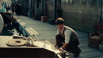 Movie still from “Dunkirk” (2017), directed by Christopher Nolan – A man kneeling down next to a boat on a dock; Medium shot, High angle