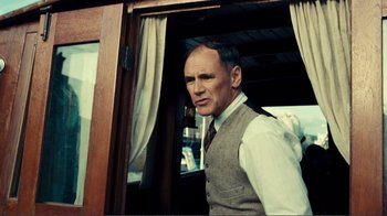 Movie still from “Dunkirk” (2017), directed by Christopher Nolan – A man in a vest and tie standing in front of a window; Medium shot, Over the shoulder angle