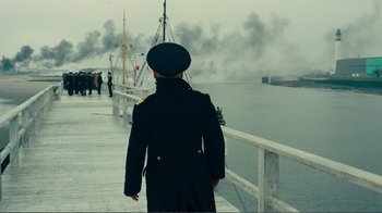 Movie still from “Dunkirk” (2017), directed by Christopher Nolan – A man in a military uniform walking on a pier; Wide shot, Over the shoulder angle