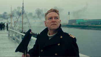 Movie still from “Dunkirk” (2017), directed by Christopher Nolan – A man in a black coat holding an umbrella in front of a body of water; Close Up shot, Low angle